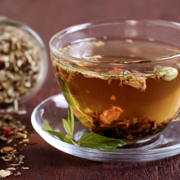 A clear cup of herbal tea with tipped over jar of dried herbs behind it.